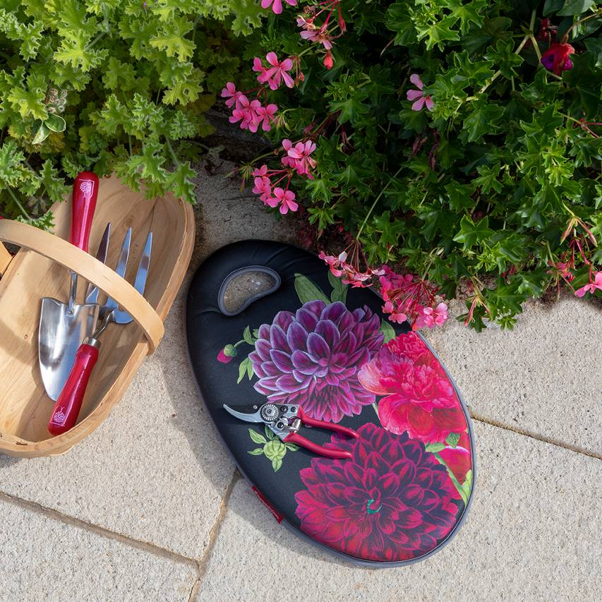 British Bloom garden kneeler with secateurs and wooden trug containing hand fork and trowel on patio next to pink geranium