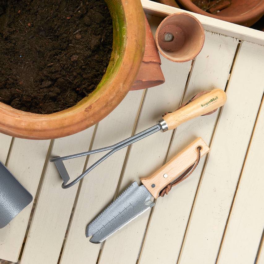 Burgon and Ball container weeder on potting bench with other hand tools and terracotta pot filled with compost