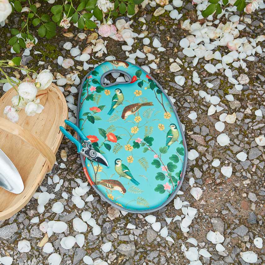 Burgon and Ball Flora and Fauna garden kneeling pad, secateurs and wooden trug on gravel next to rose bushes with scattered petals