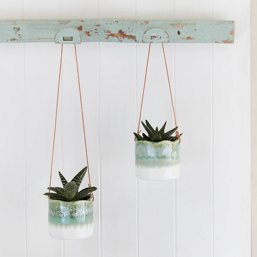 Two wave hanging pots with succulents against white panelled background