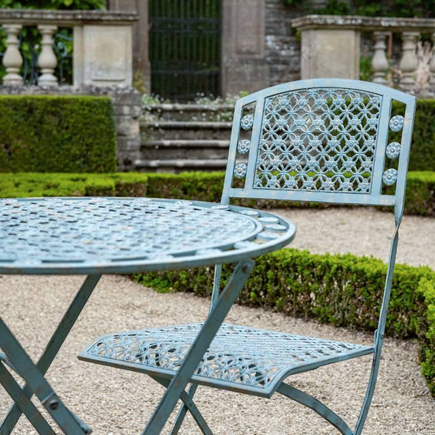 Marlborough 3 piece bistro set in vintage green on gravel in front of box hedging and stone steps leading to wrought iron gate