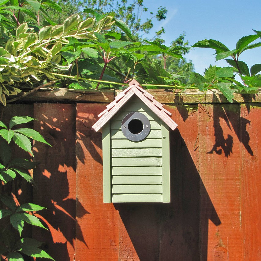 Frontview of New England nestbox in sage green attached to wooden fence in bright sunlight